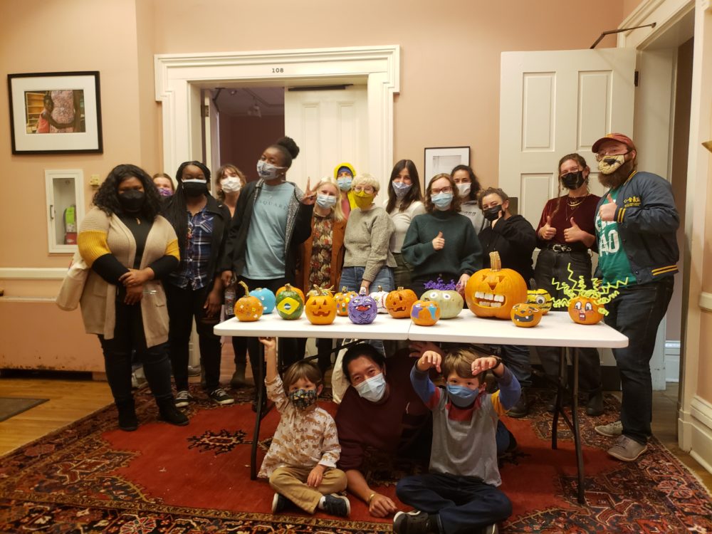 students stand behind table of decorated pumpkins