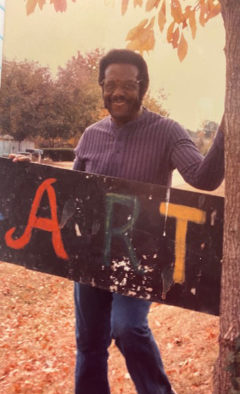 Man stands with large painted sign that says Art.