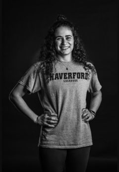 Curly haired girl standing with hands on her hips wearing a gray Haverford Lacrosse t-shirt