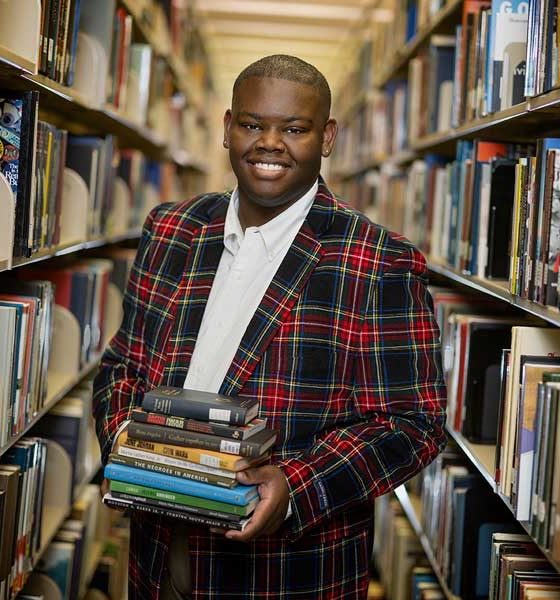 Jalon poses in a library while holding books