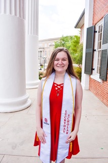 Girl in red dress with honors regalia standing in front of the Lyceum